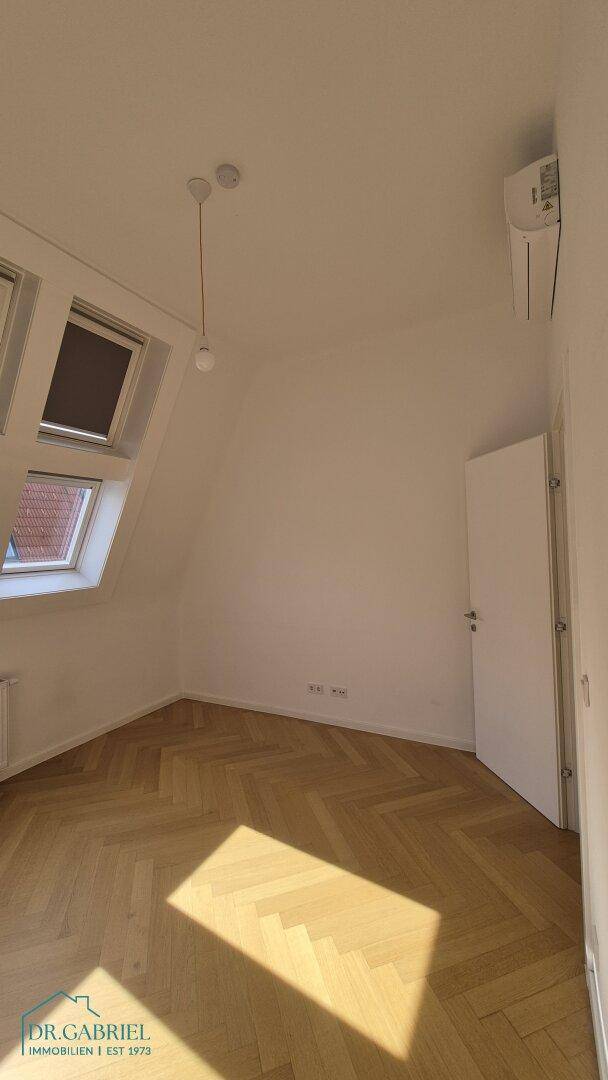 Heller Raum mit Fischgrätparkett, Dachfenstern und einer installierten Klimaanlage.