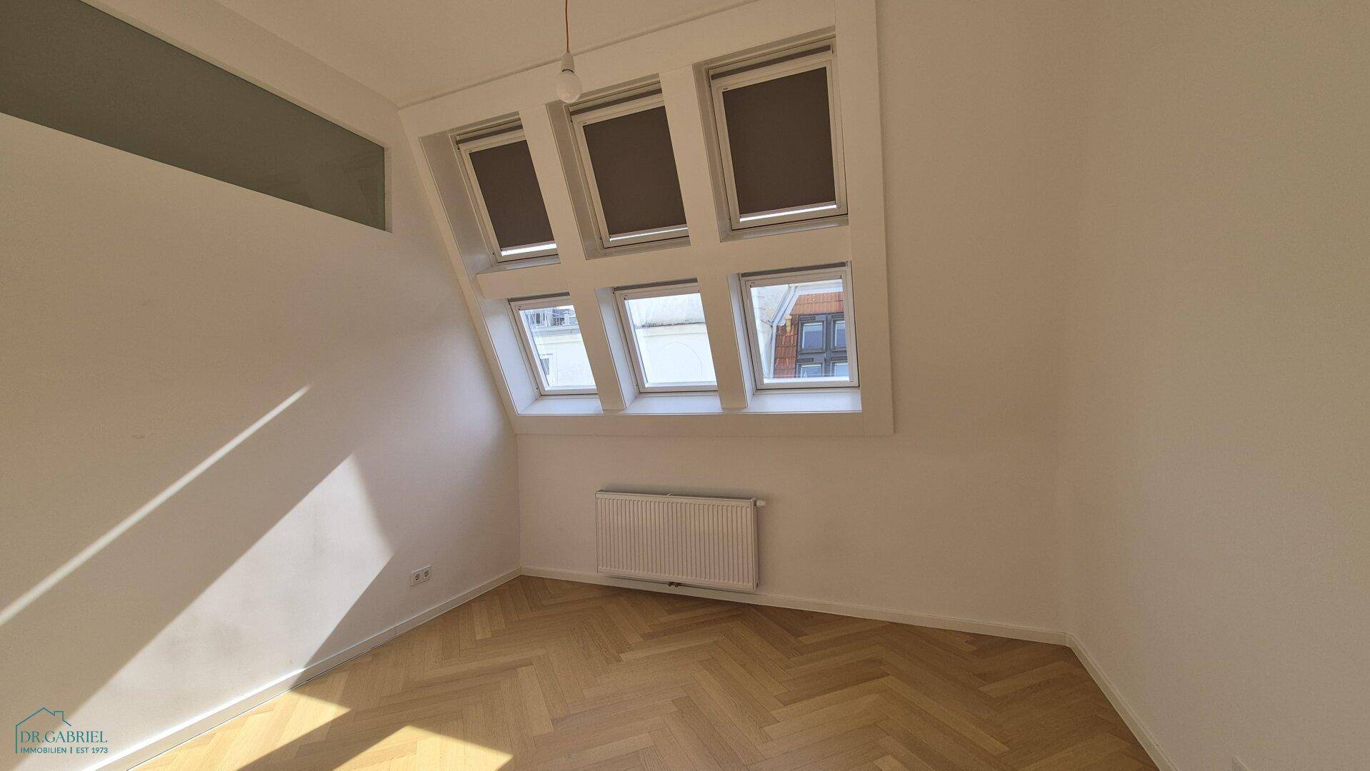 Geräumiger Raum mit Fischgrätparkett und Dachfenstern, die viel Tageslicht hereinlassen.