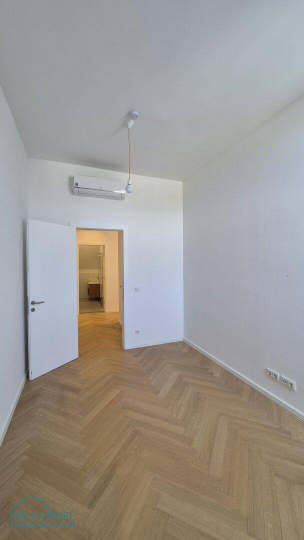 Heller Raum mit Fischgrätparkett und Klimaanlage, mit Zugang zu einem weiteren Zimmer.