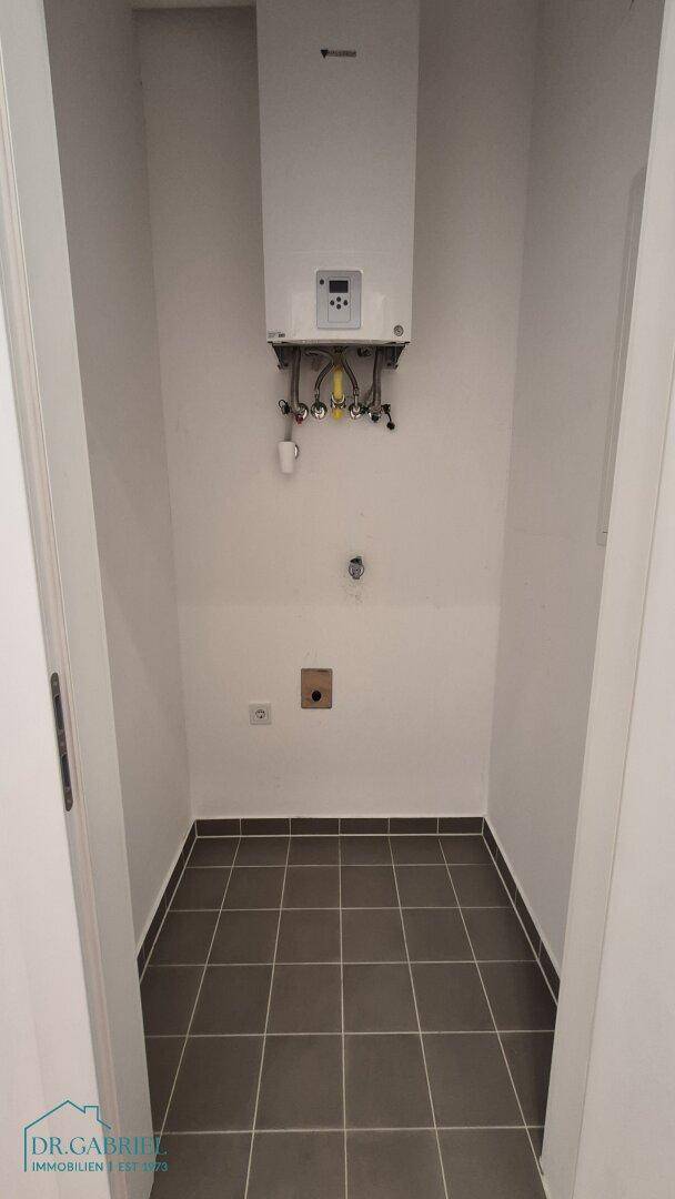 Kleiner Hauswirtschaftsraum mit Boiler und dunklen Fliesen, ideal für Technik und Lagerung.