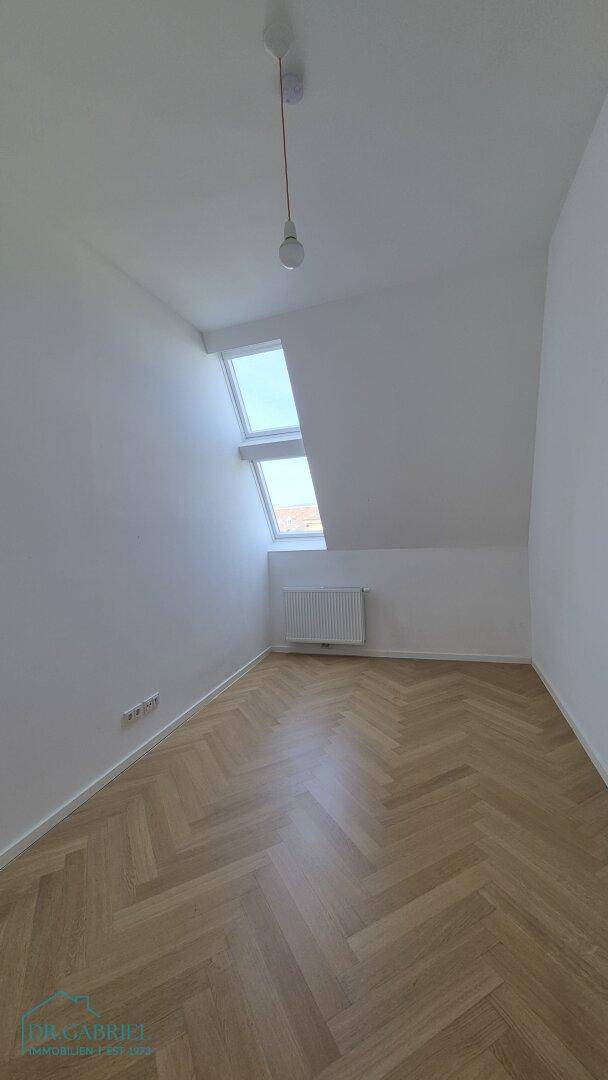 Heller Raum mit Fischgrätparkett, Dachfenstern und einem Heizkörper, ideal als Kinderzimmer.