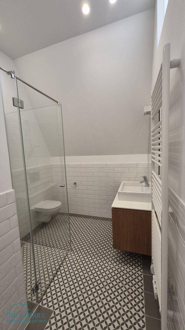 Modernes Badezimmer mit begehbarer Dusche, gemusterten Fliesen und beheiztem Handtuchhalter.