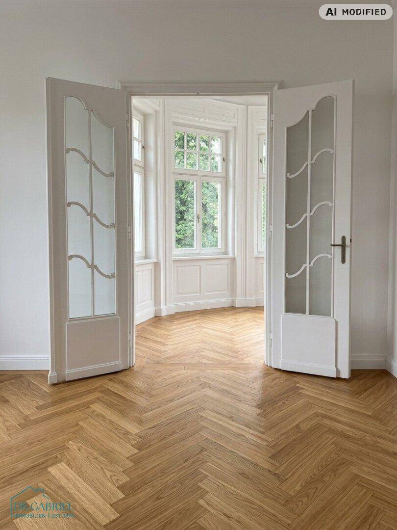 Heller Raum mit eleganten Flügeltüren und Fischgrätparkett, der zu einem lichtdurchfluteten Erkerbereich führt.