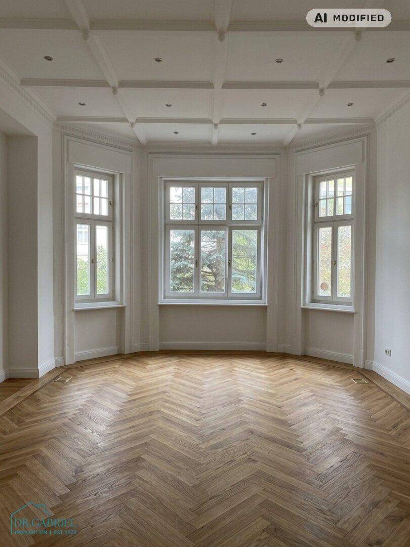 Geräumiger Wohnbereich mit Fischgrätparkett, hohen Decken und einem großen Erkerfenster.