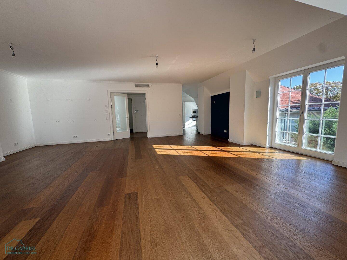 Heller Wohnbereich mit Holzboden und Zugang zu weiteren Räumen sowie einem Fenster.