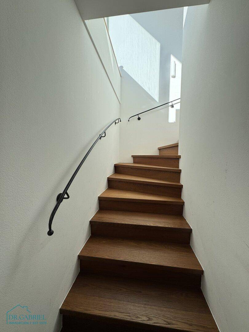 Elegante Holztreppe mit schwarzem Handlauf und viel natürlichem Licht von oben.