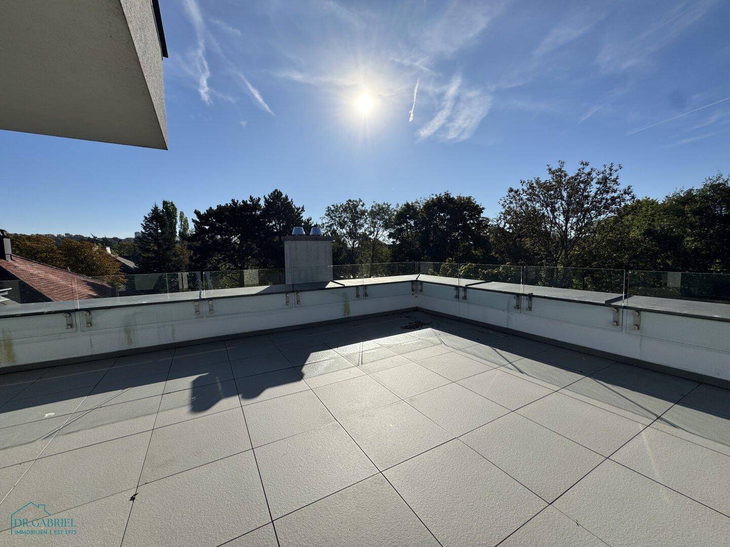 Geräumige Dachterrasse mit Fliesenboden und Glasgeländer, bietet weite Ausblicke ins Grüne.