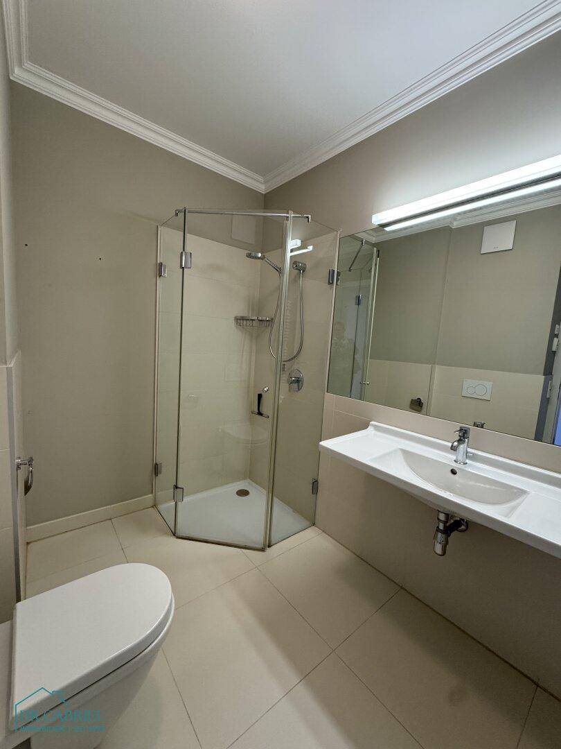 Modernes Badezimmer mit Duschkabine, wandhängendem WC und Einzelwaschbecken auf hellen Fliesen.