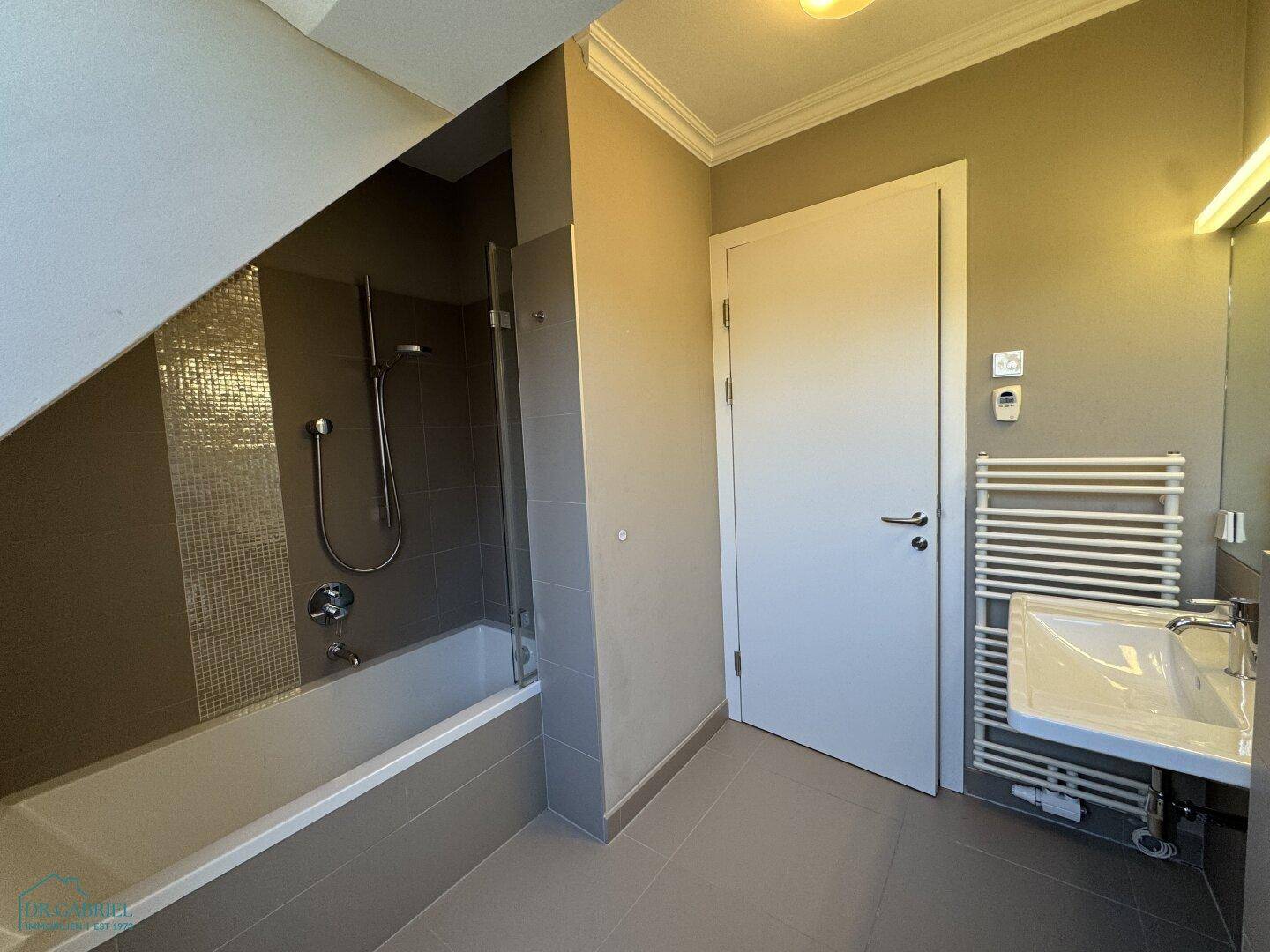 Modernes Badezimmer mit Badewanne, Dusche, Waschbecken und beheiztem Handtuchhalter.