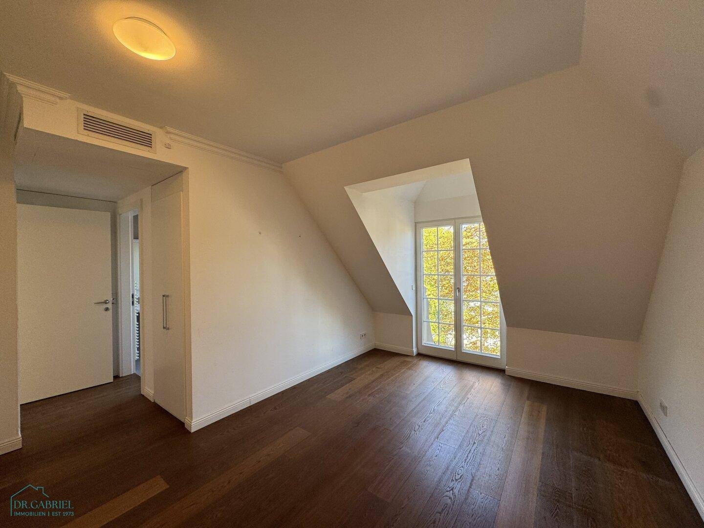 Geräumiges Zimmer mit Holzboden, Einbauschrank und französischem Balkon im Dachgeschoss.
