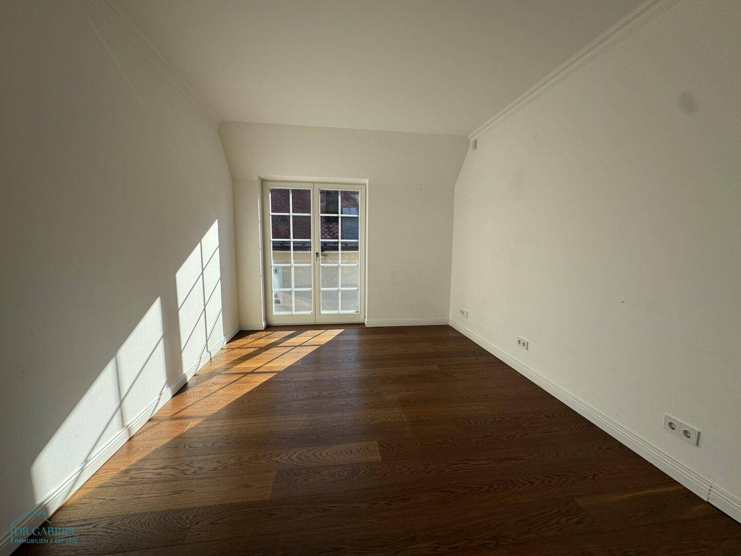 Helles, leeres Zimmer mit Holzboden und französischem Balkon, ideal als Schlaf- oder Arbeitszimmer.