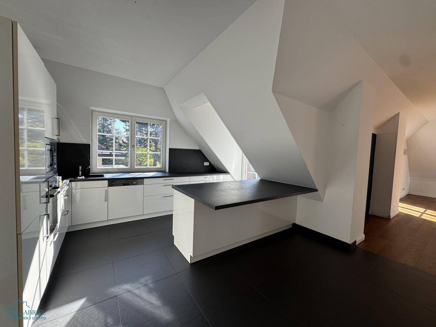 Moderne Küche im Dachgeschoss mit weißen Hochglanzfronten, dunklen Arbeitsplatten und Fliesenboden.