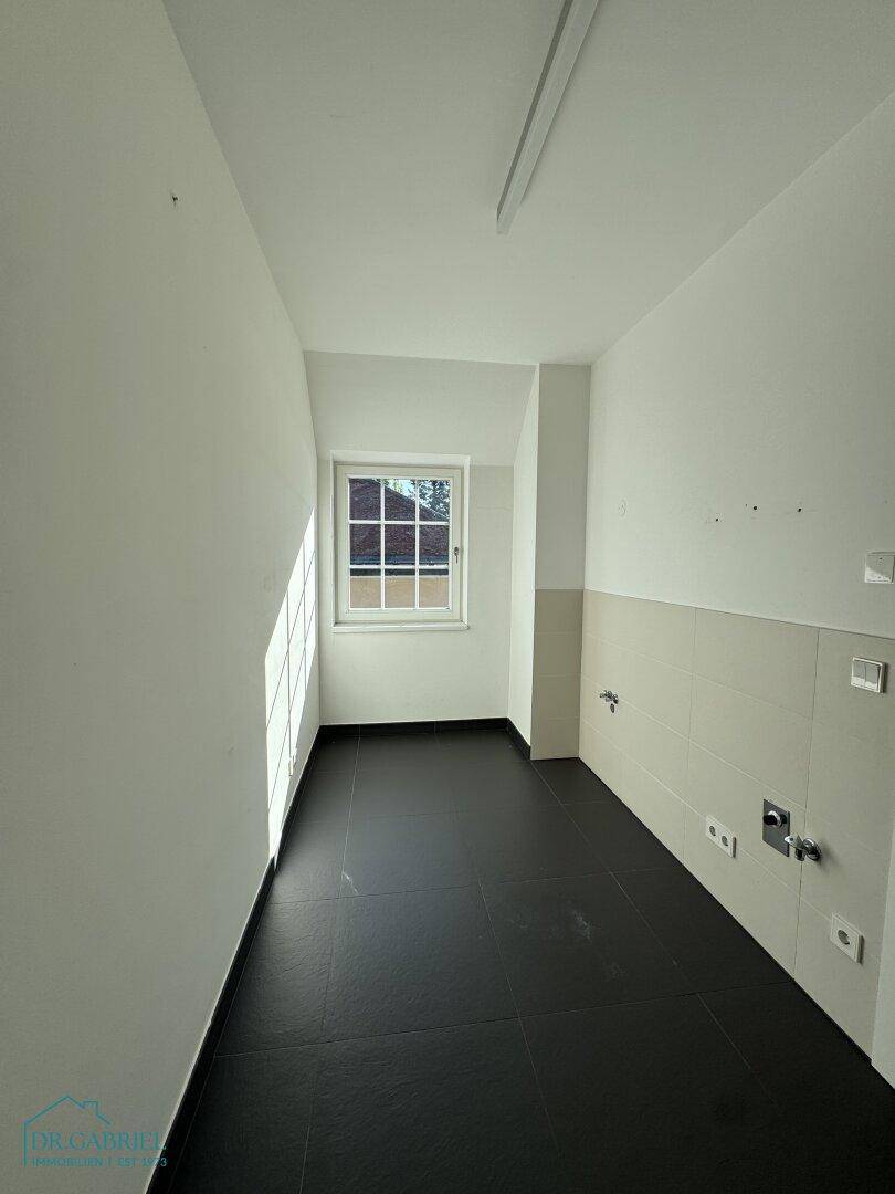 Praktischer Hauswirtschaftsraum mit Fliesenboden, teilgefliesten Wänden und einem Fenster.