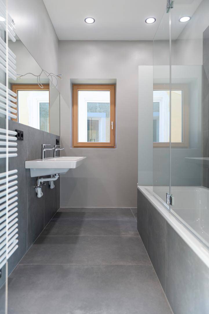 Modernes Badezimmer mit grauen Fliesen, Badewanne, Einzelwaschbecken und Fenster.