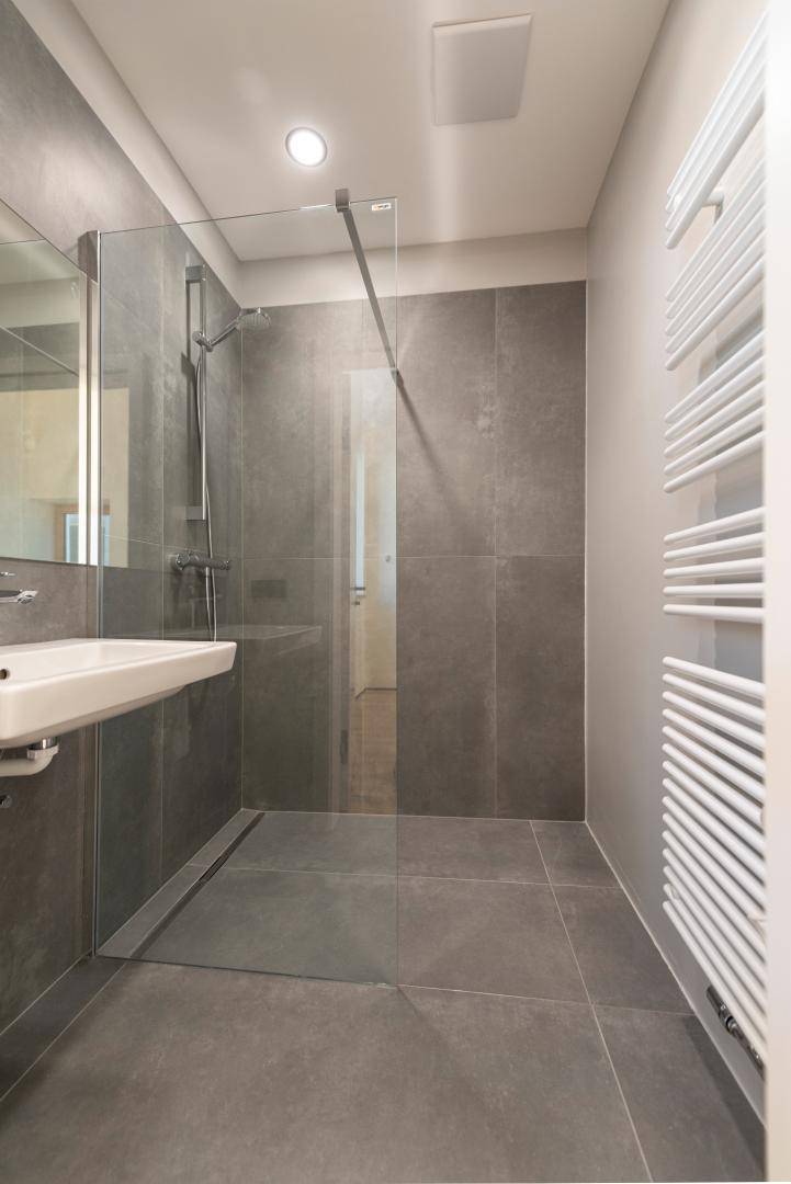 Modernes Badezimmer mit grauen Fliesen, begehbarer Dusche, Einzelwaschbecken und Handtuchheizkörper.