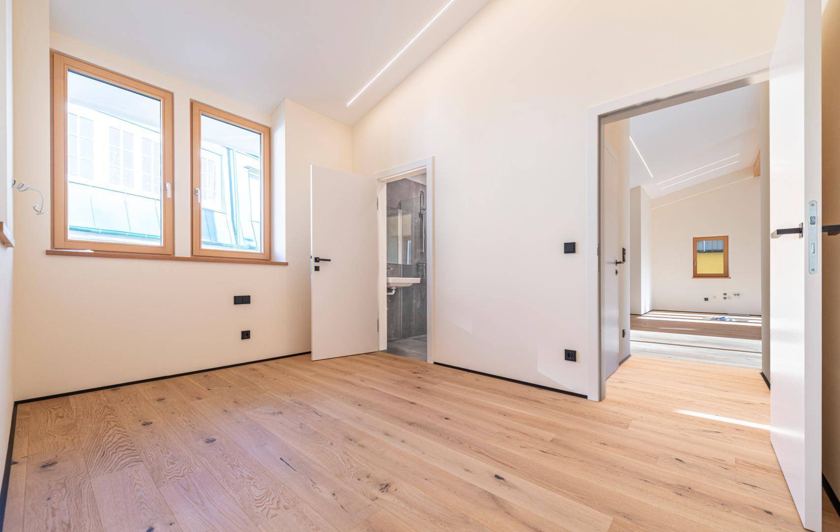 Unmöbliertes Schlafzimmer mit Holzboden, drei Fenstern und Zugang zu einem Badezimmer.