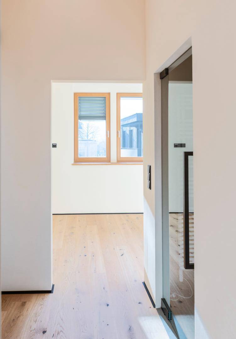 Heller Raum mit Holzfenstern und Holzboden, gesehen durch eine offene Tür.