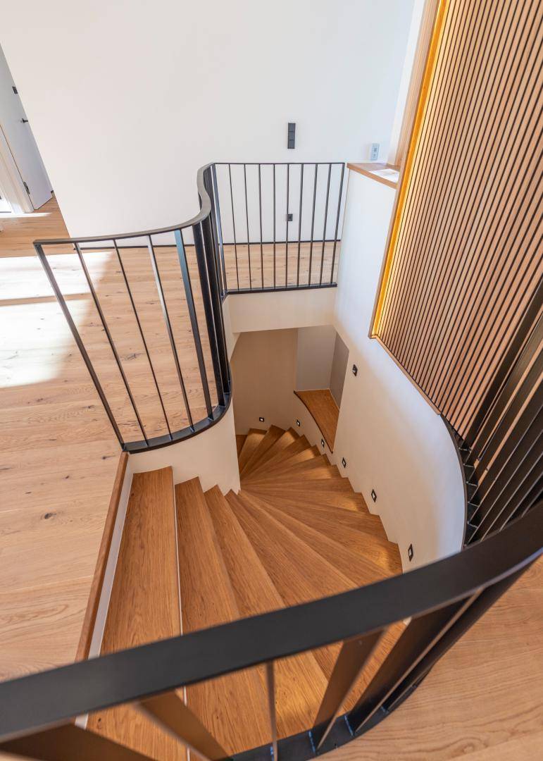 Elegante geschwungene Holztreppe mit schwarzem Metallgeländer und integrierter Beleuchtung.