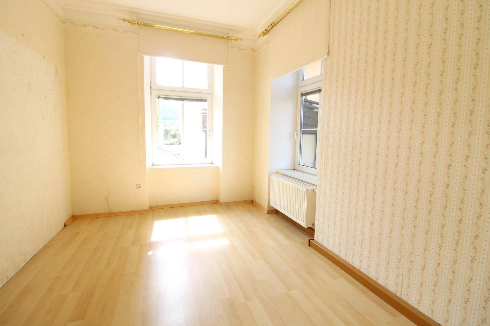 Helles Zimmer mit Holzboden und gemusterter Tapete, ideal als Schlaf- oder Arbeitszimmer.