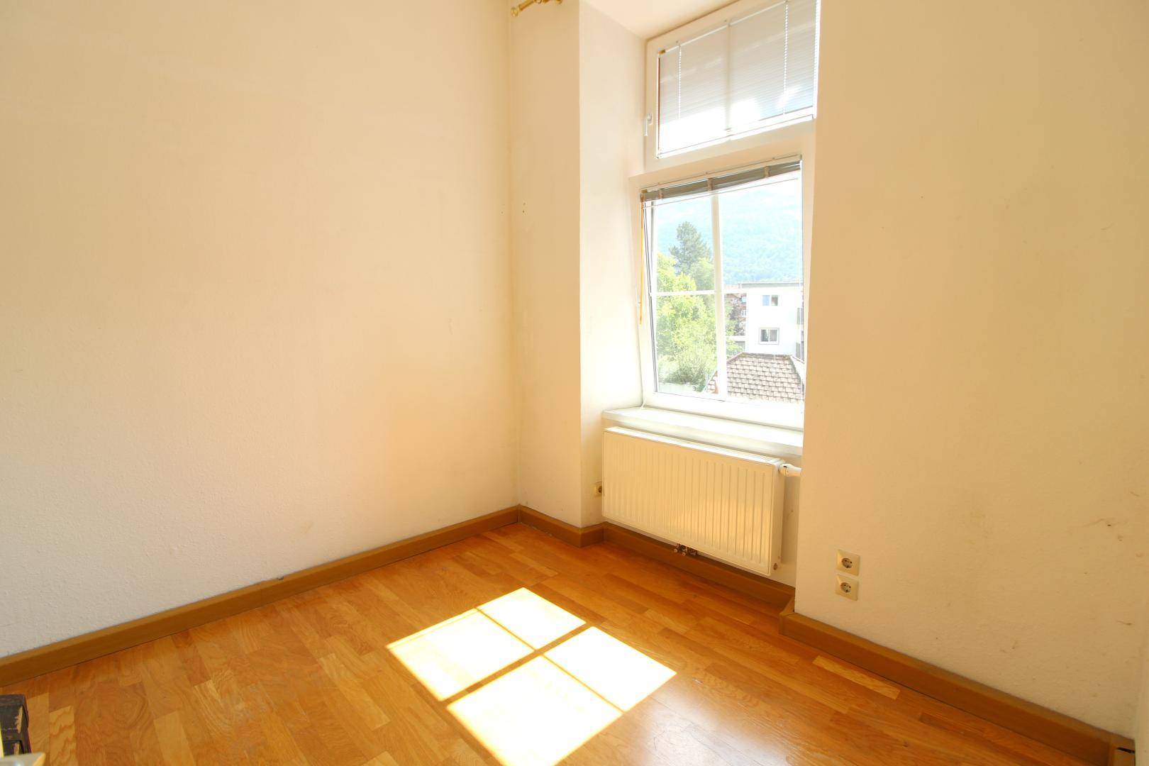Helles Schlafzimmer mit Holzboden und einem Fenster mit Blick auf die Berge.