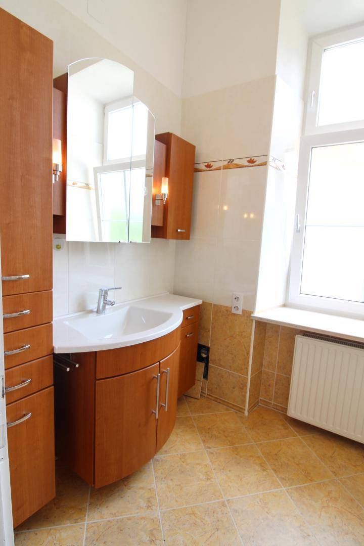 Badezimmer mit Fenster, Einzelwaschbecken und hellbraunen Fliesen.