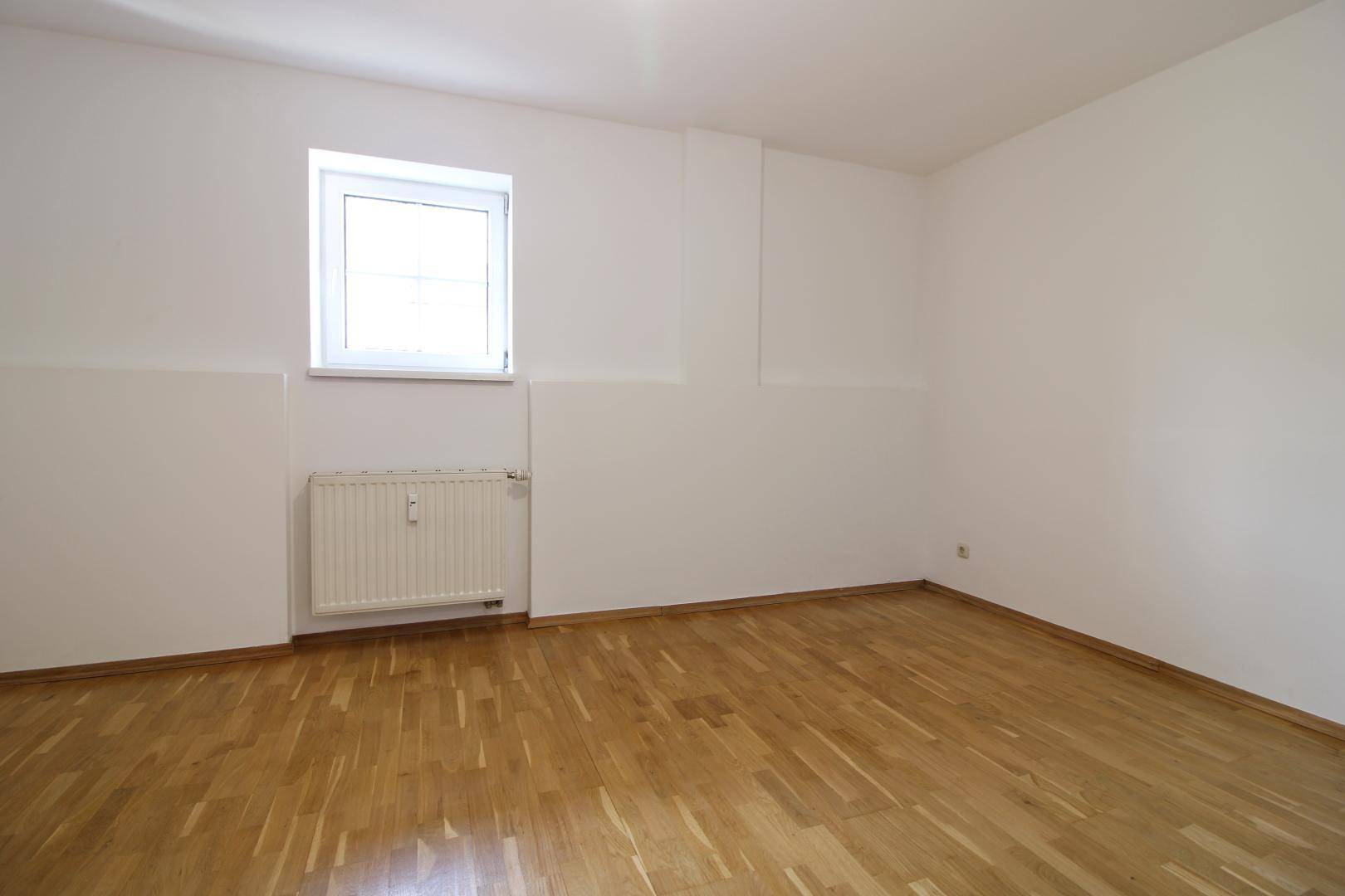 Ruhiges Schlafzimmer mit Holzboden und einem Fenster, das viel Tageslicht hereinlässt.