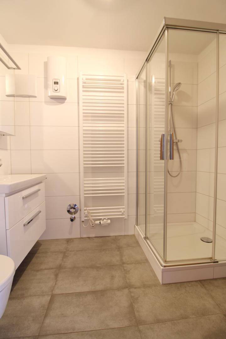 Modernes Badezimmer mit Duschkabine, Waschbecken und beheiztem Handtuchhalter.