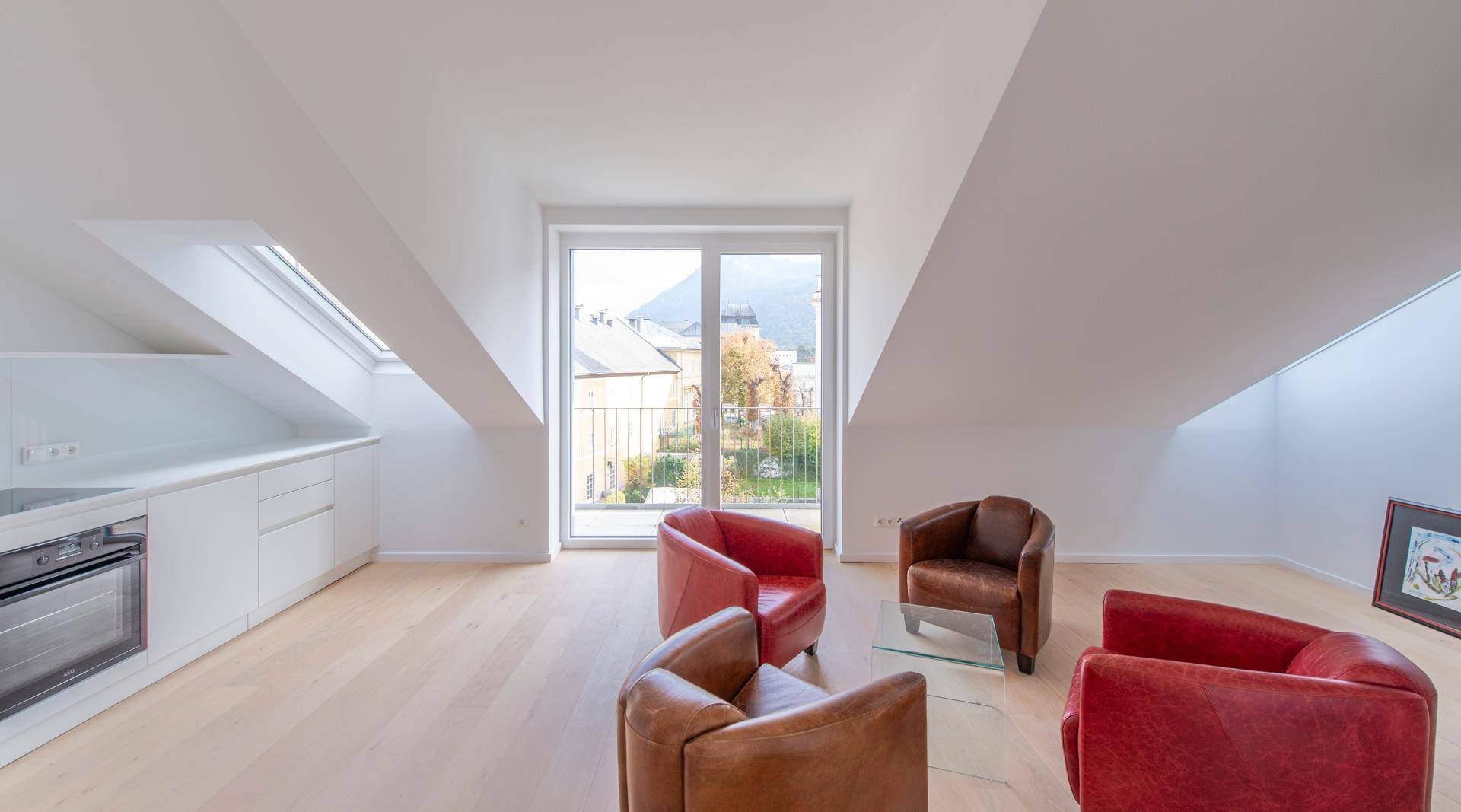 Heller Wohnbereich im Dachgeschoss mit integrierter Küchenzeile, Holzboden und Zugang zu einem kleinen Balkon.