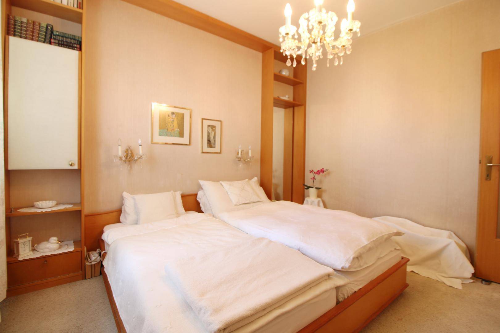 Helles Schlafzimmer mit zwei Einzelbetten, Holzregalen und einem eleganten Kronleuchter.
