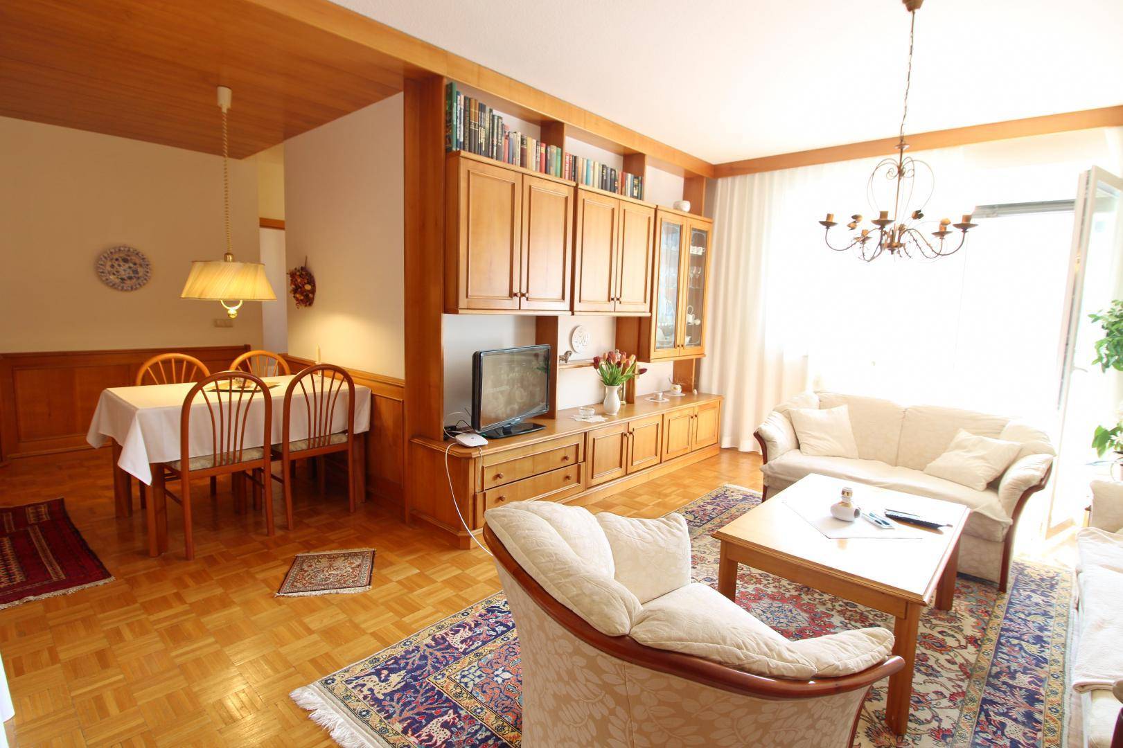 Gemütlicher Wohn-Essbereich mit Parkettboden, traditionellen Möbeln und Zugang zum Balkon.