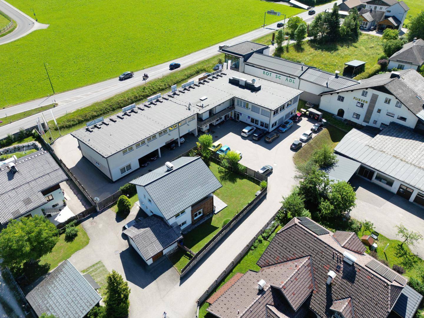 Vogelperspektive auf ein Gewerbegebäude mit angrenzenden Wohnhäusern und grünen Feldern.