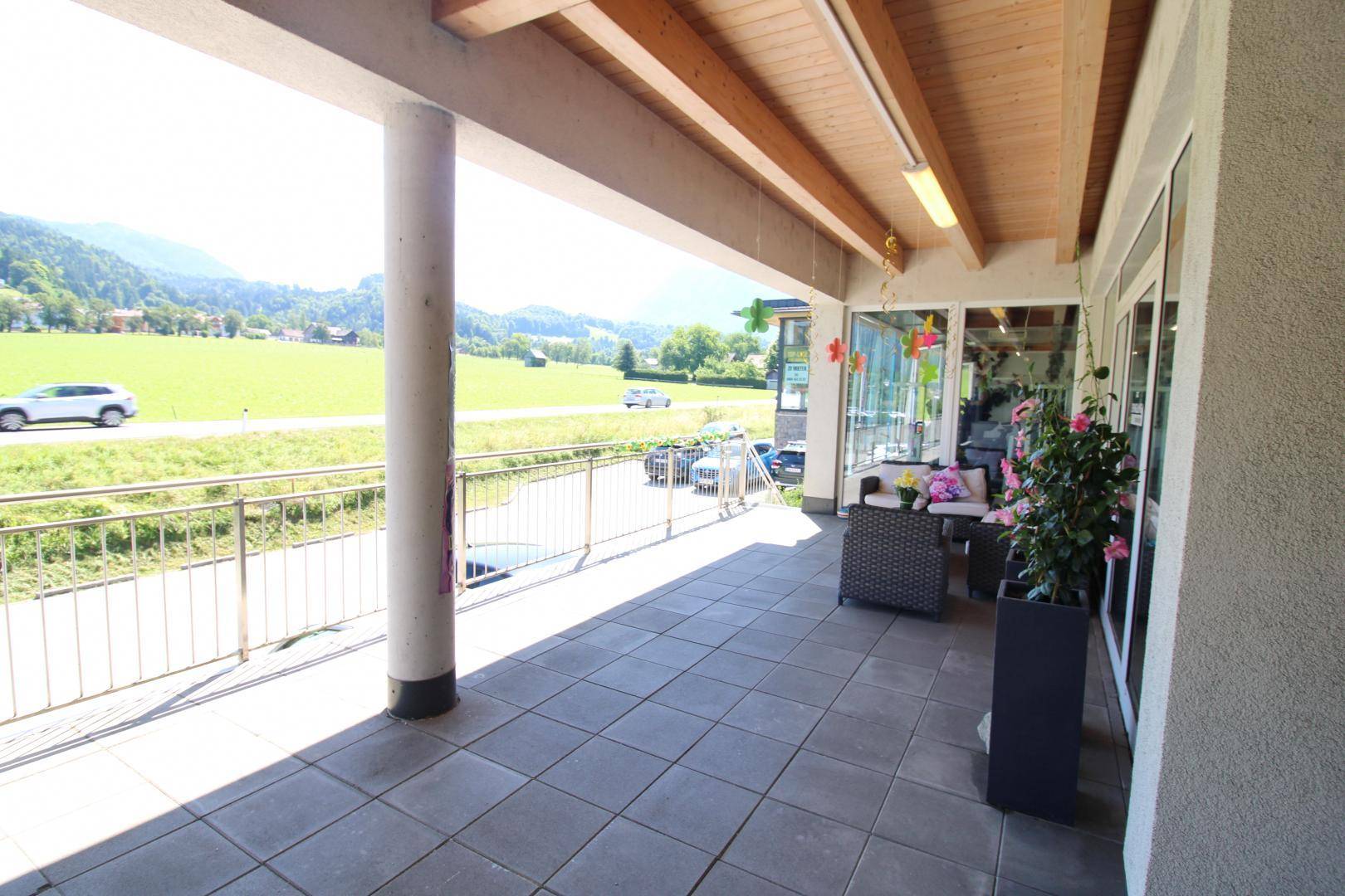 Sonniger überdachter Terrassenbereich mit Sitzgelegenheiten und weitem Blick auf die Landschaft.