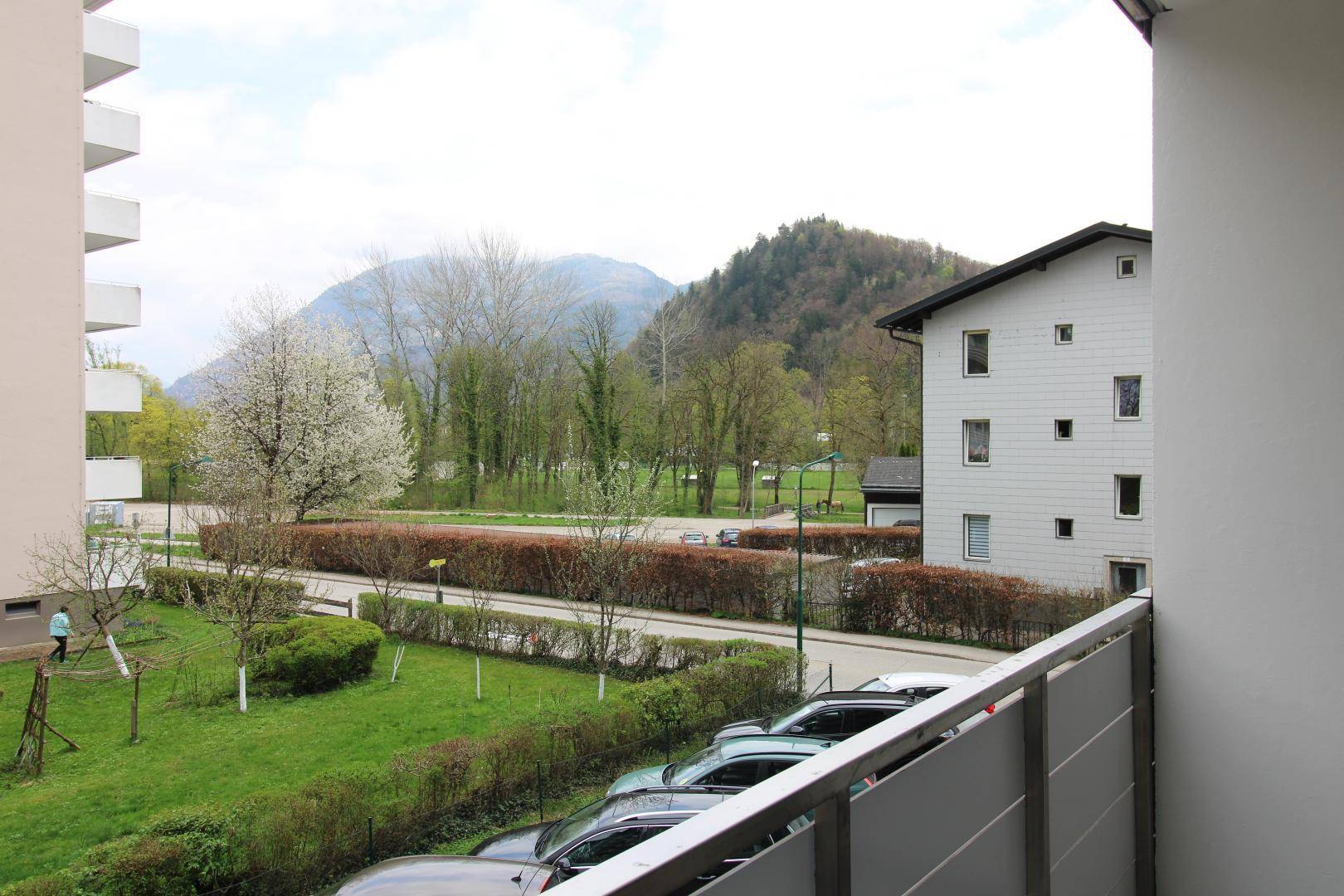 Balkon mit Bergblick und Aussicht auf die grüne Umgebung und einen Parkplatz.