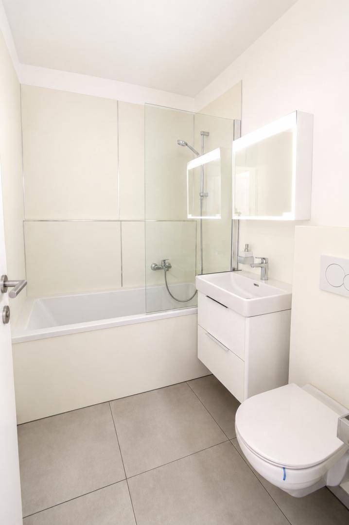Helles Badezimmer mit Badewanne, wandhängendem WC und modernem Waschtisch mit Spiegel.