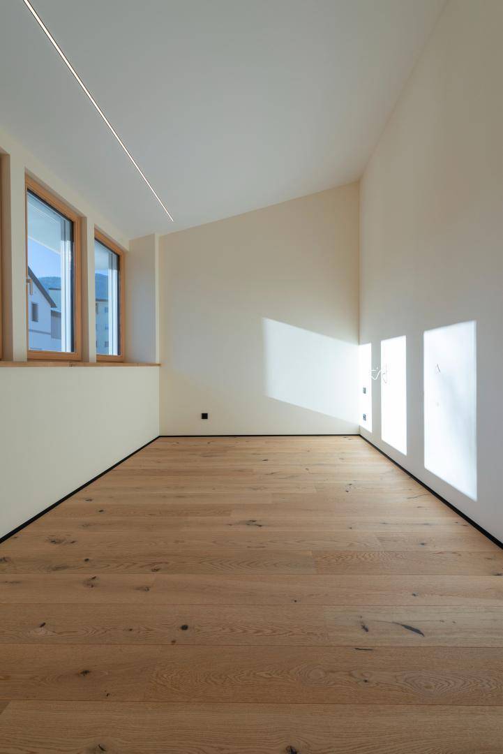 Leerer Raum mit Holzboden, schrägen Wänden und großen Fenstern für viel Tageslicht.