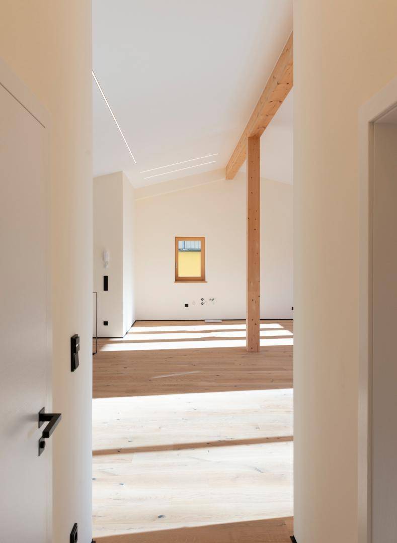 Heller Flur führt in einen geräumigen Raum mit Holzbalken und hohen Decken.