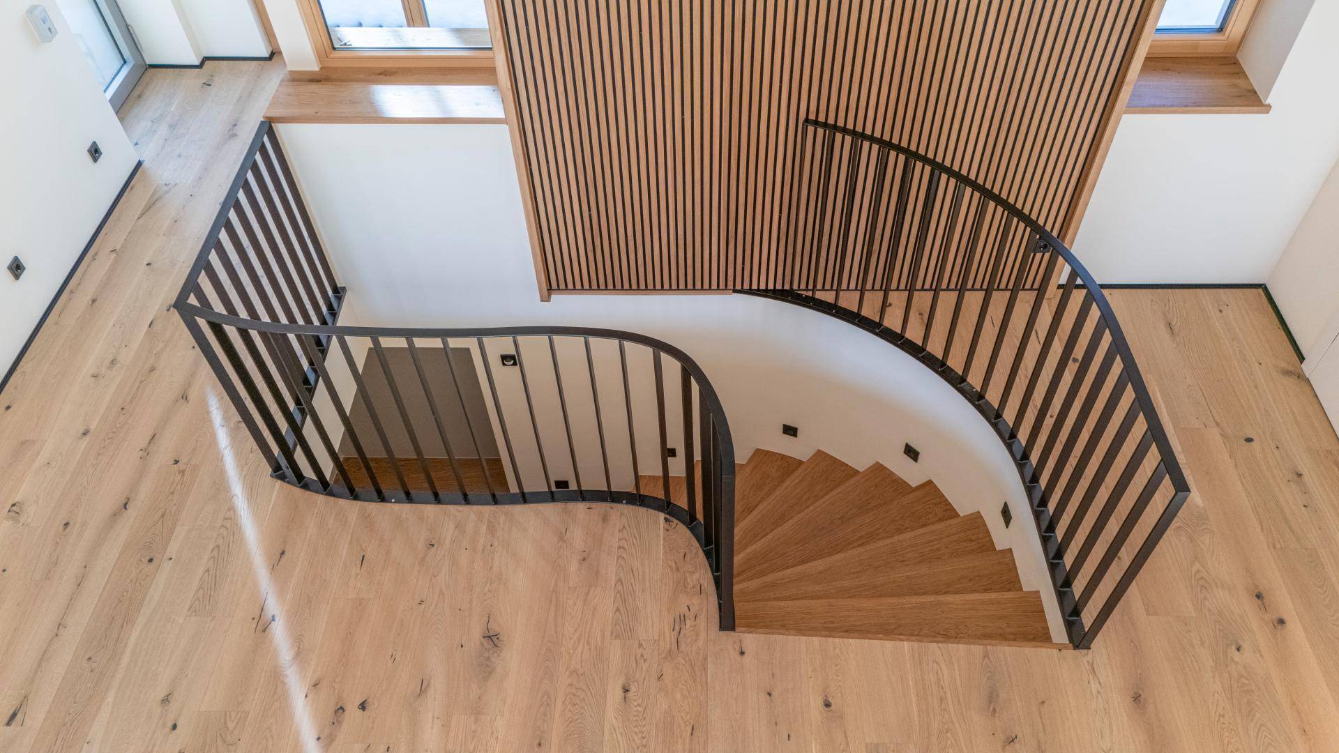 Elegante geschwungene Holztreppe mit modernem Geländer und Holzvertäfelung.
