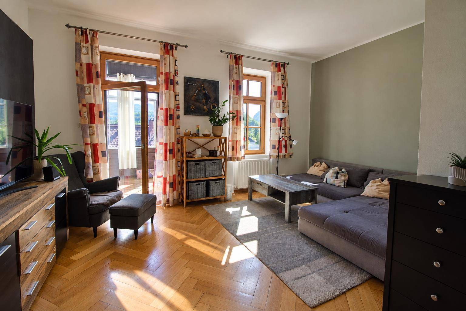 Helles Wohnzimmer mit Fischgrätparkett, gemütlicher Sitzecke und Balkonzugang.