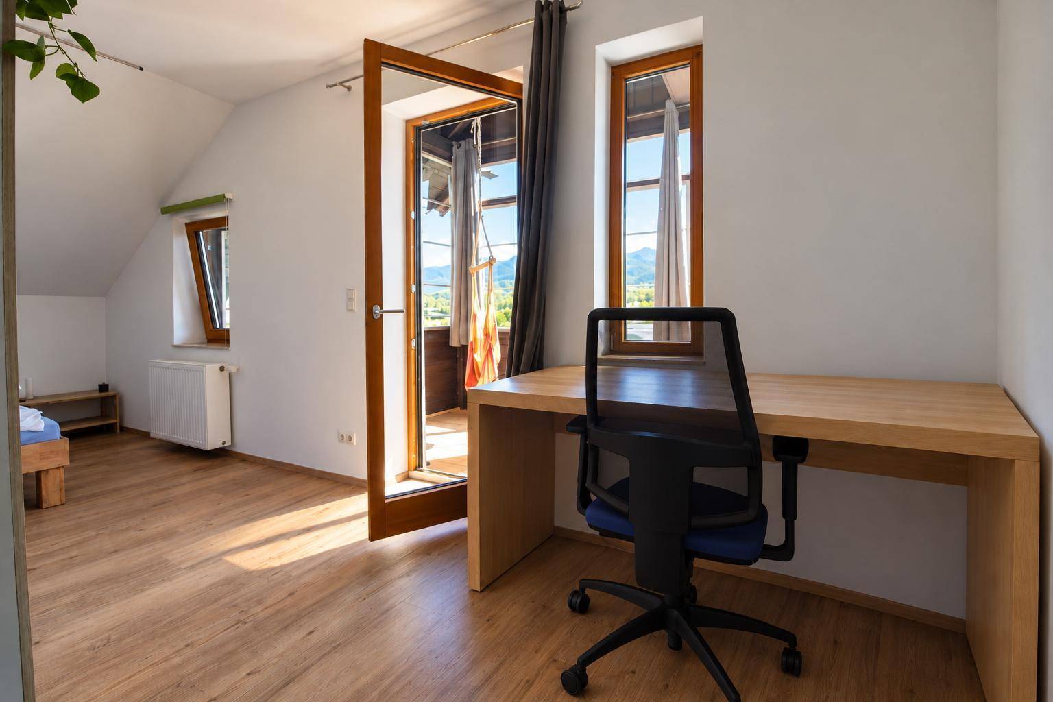 Helles Schlafzimmer mit Schreibtisch, Laminatboden und Zugang zu einem sonnigen Balkon.