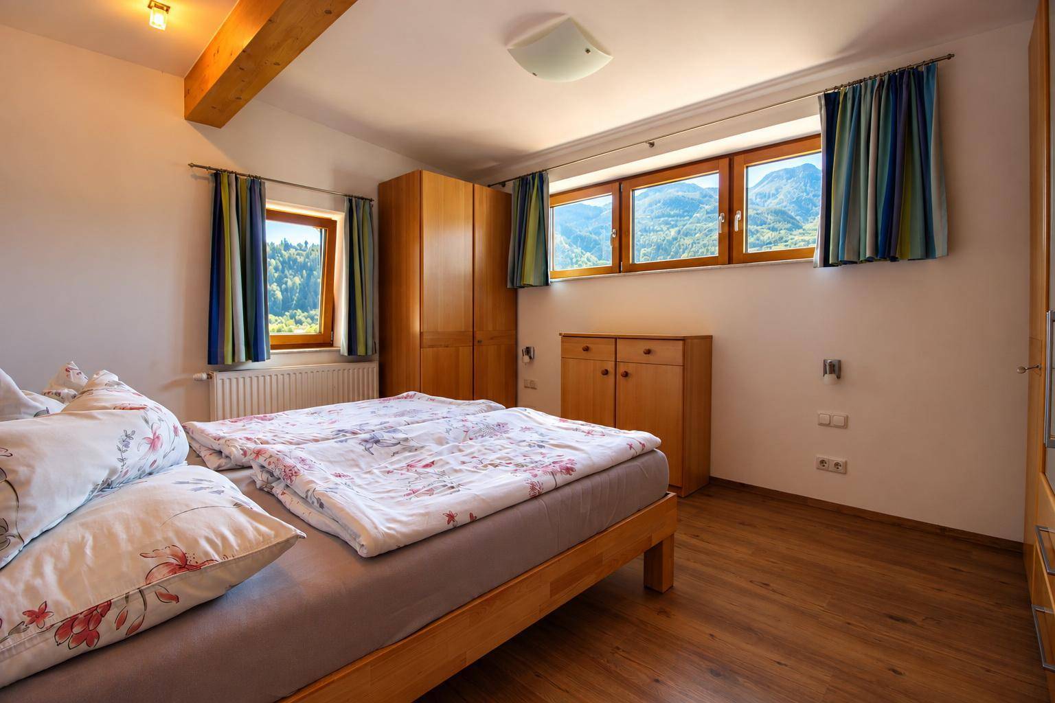 Helles Schlafzimmer mit Holzbalken, Laminatboden und Panoramablick auf die Berge.
