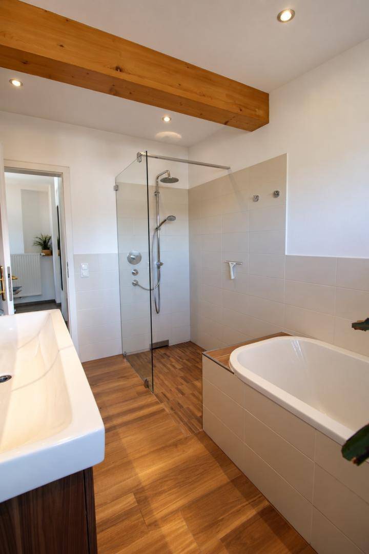 Modernes Badezimmer mit begehbarer Dusche, Badewanne und Holzbalken.