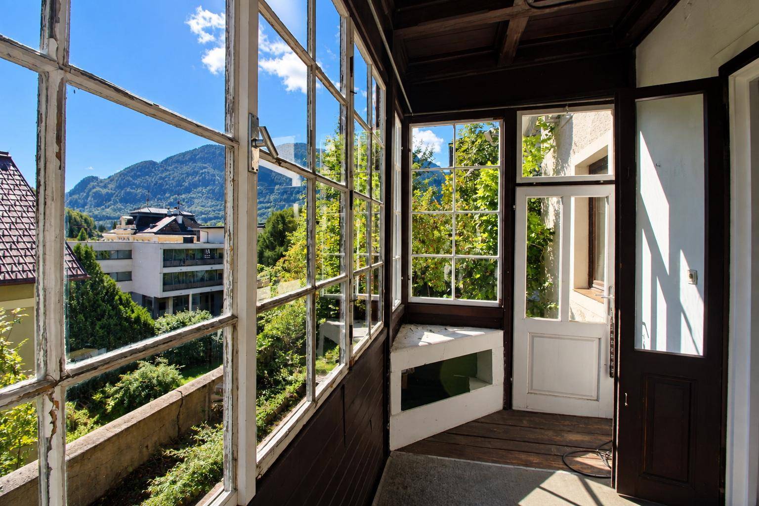 Heller Wintergarten mit vielen Fenstern, Bergblick und traditionellen Holzelementen.