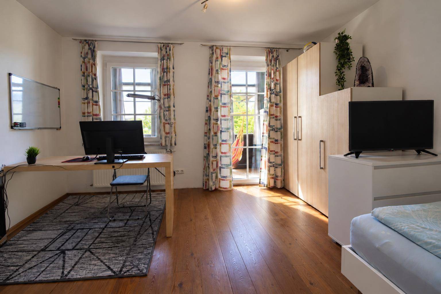 Geräumiges Schlafzimmer mit Arbeitsbereich, Laminatboden und Zugang zu einem Balkon.