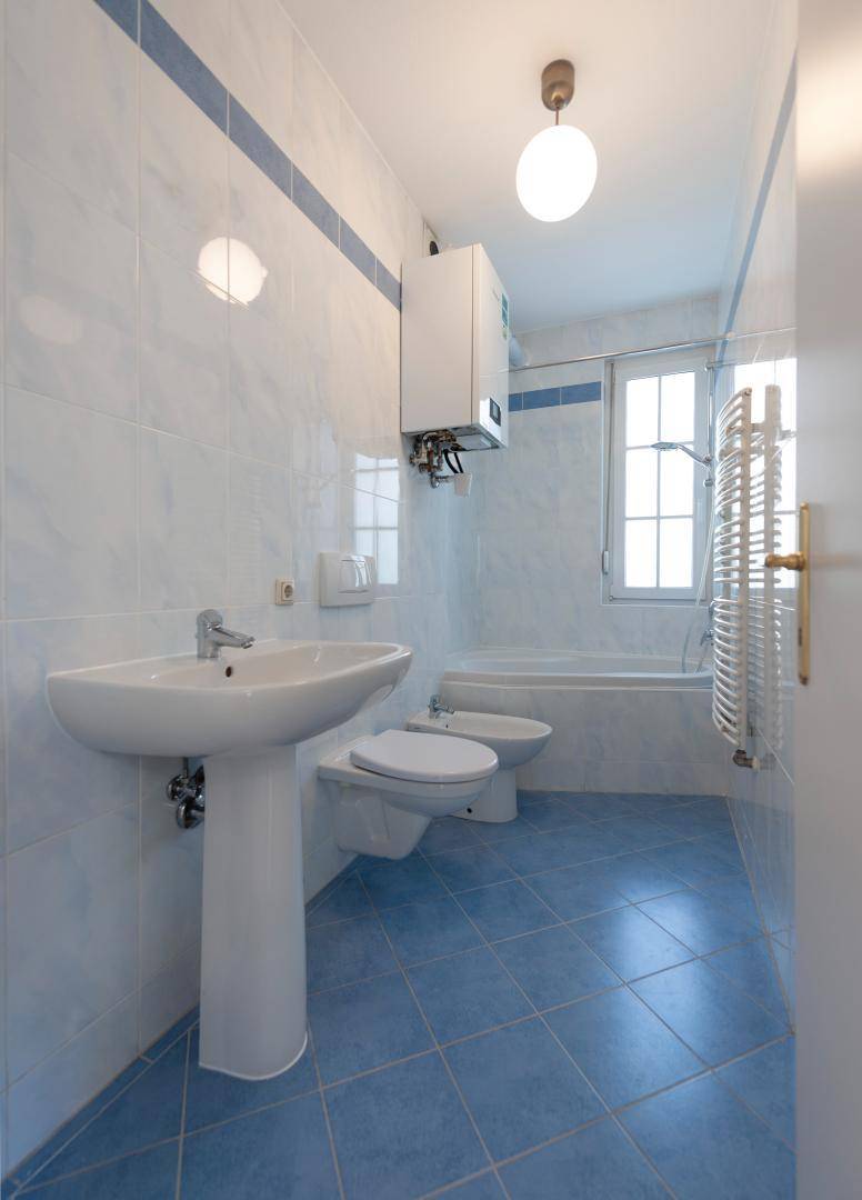 Badezimmer mit blauen Bodenfliesen, weiß gefliesten Wänden, Badewanne, Bidet und Fenster.