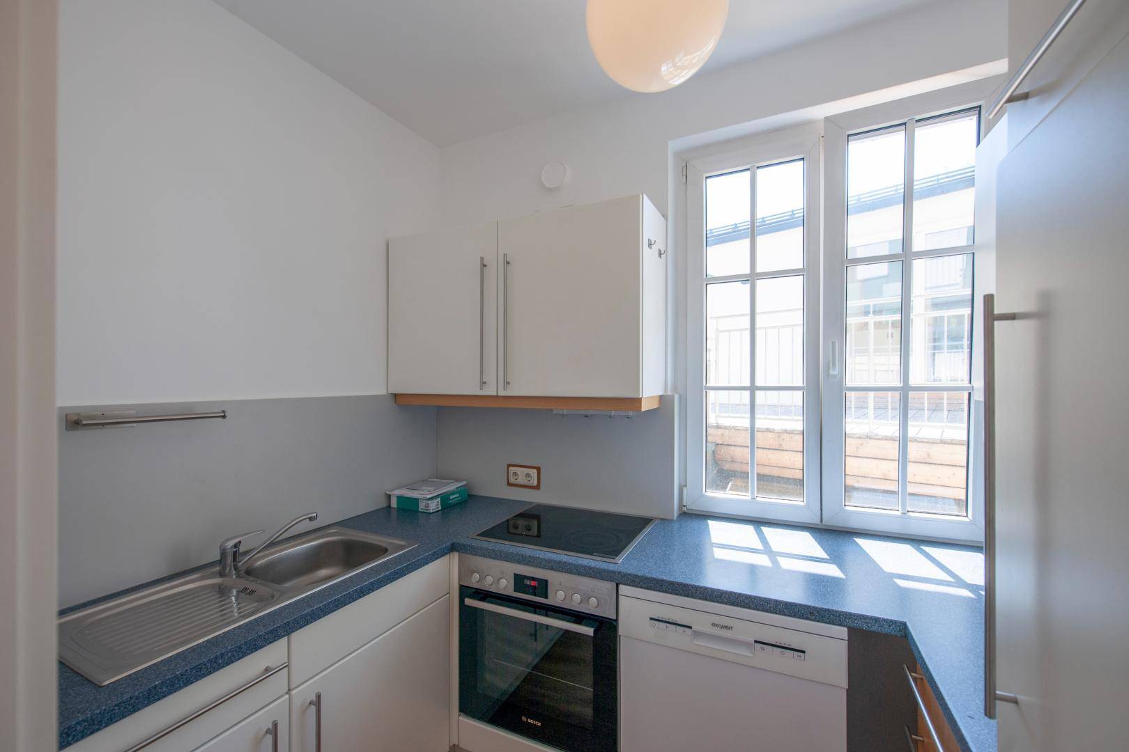 Kleine Einbauküche mit weißen Schränken, blauer Arbeitsplatte und Fenster für natürliches Licht.