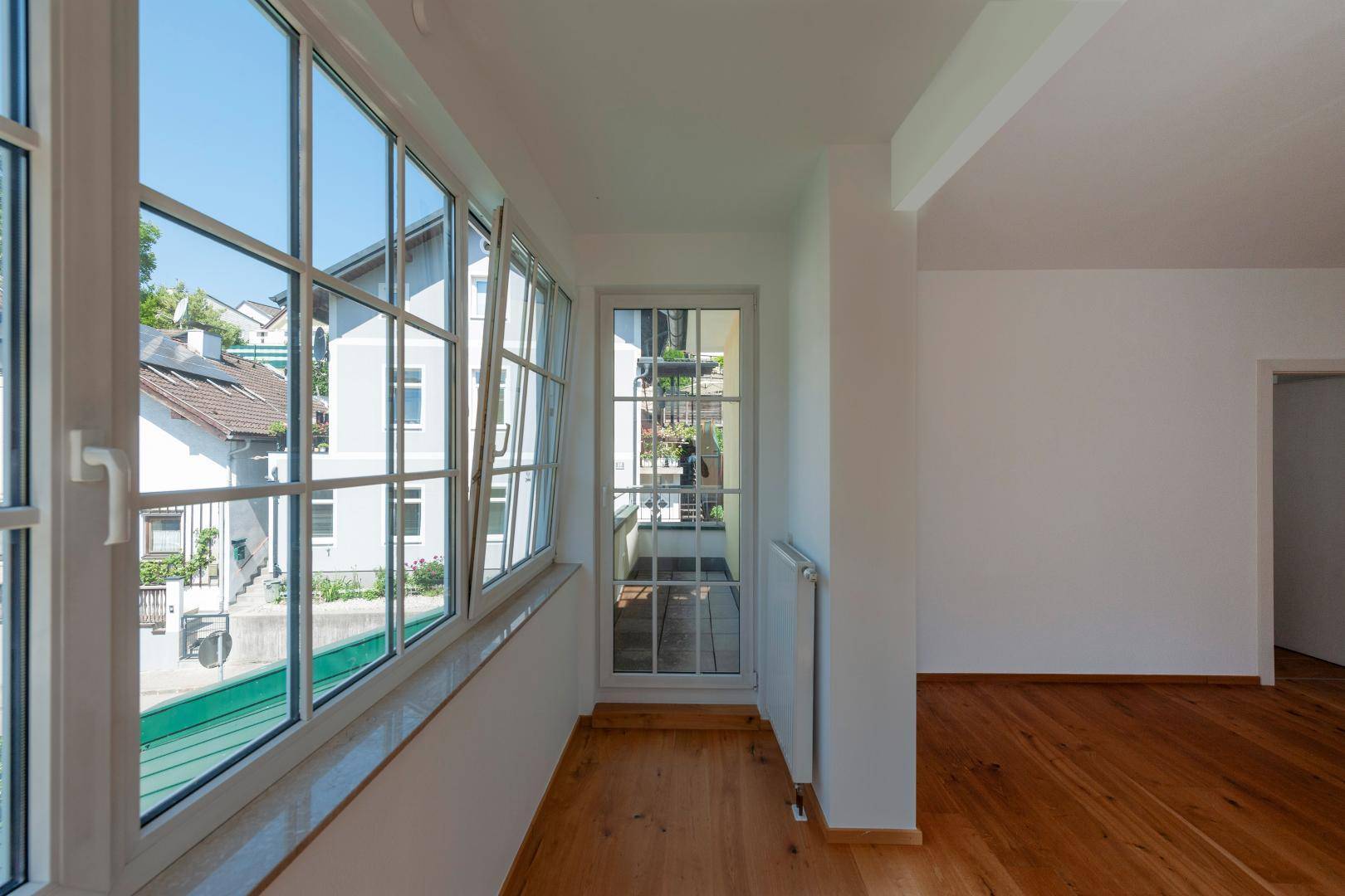 Helles Zimmer mit Holzboden, großen Fenstern und Zugang zu einem französischen Balkon.