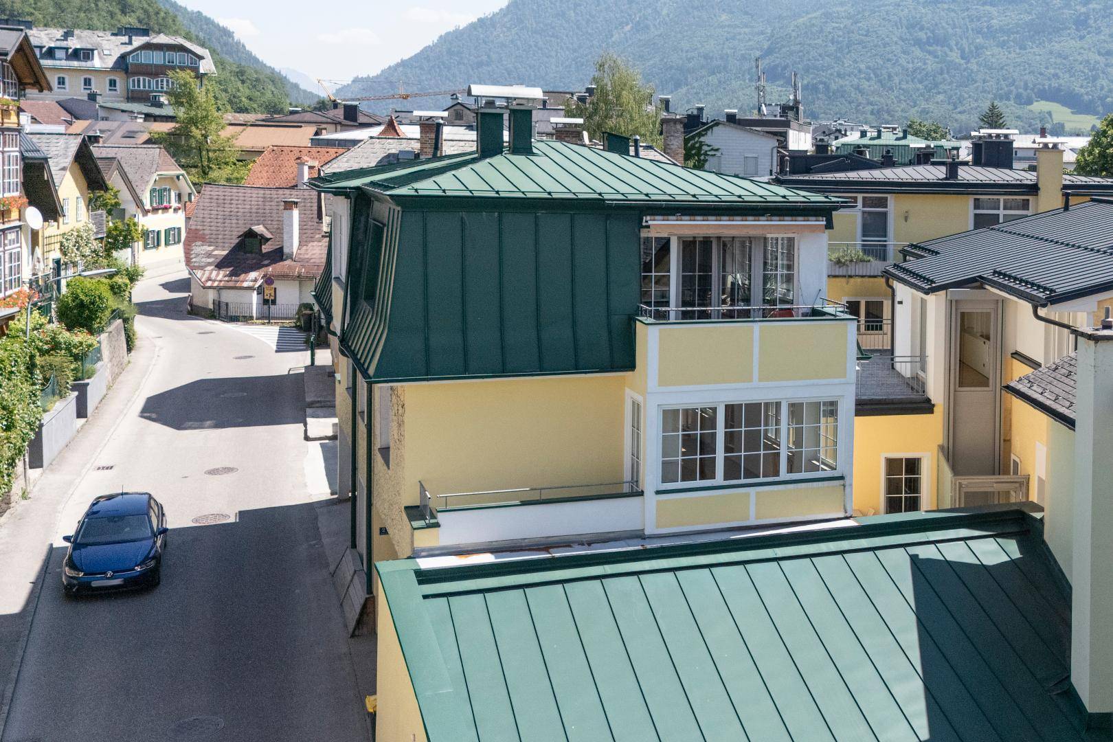 Außenansicht eines Gebäudes mit grünem Dach, Balkon und Blick auf die umliegende Berglandschaft.