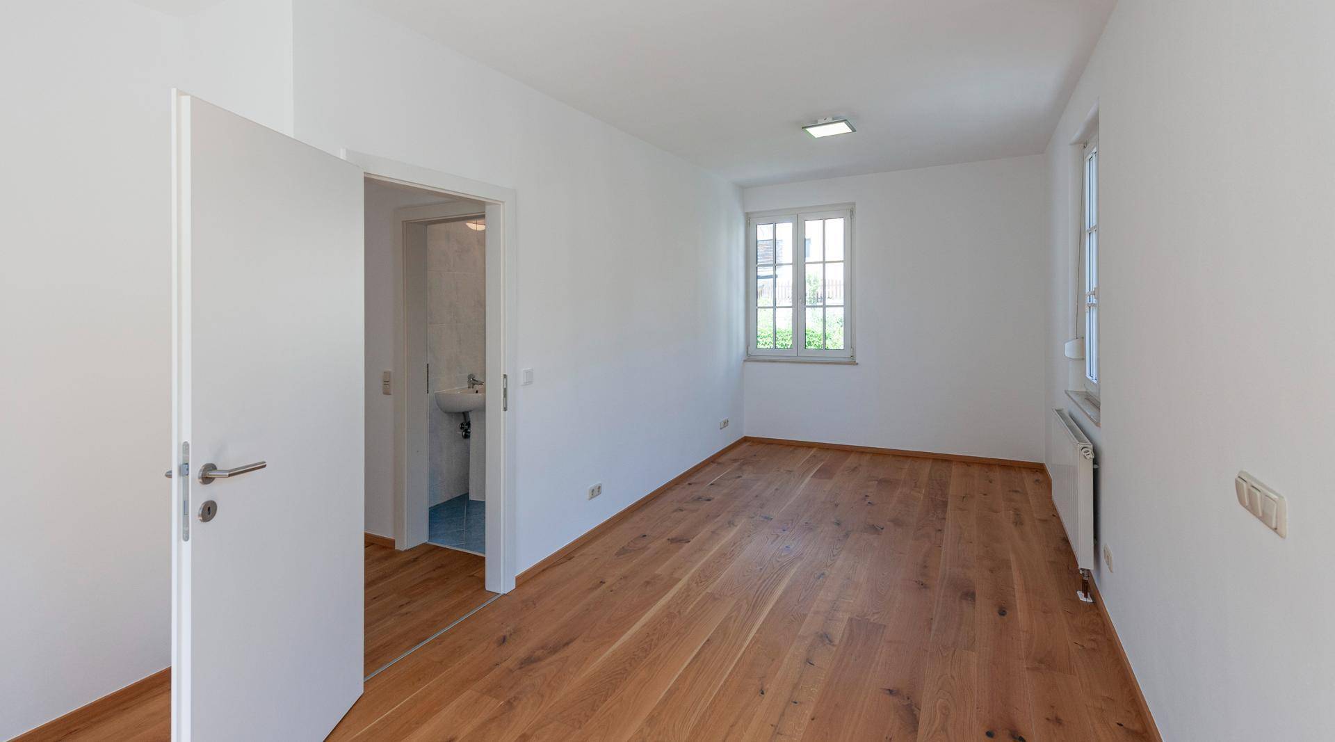 Leeres Zimmer mit Holzboden und Zugang zu einem kleinen Badezimmer oder Gäste-WC.
