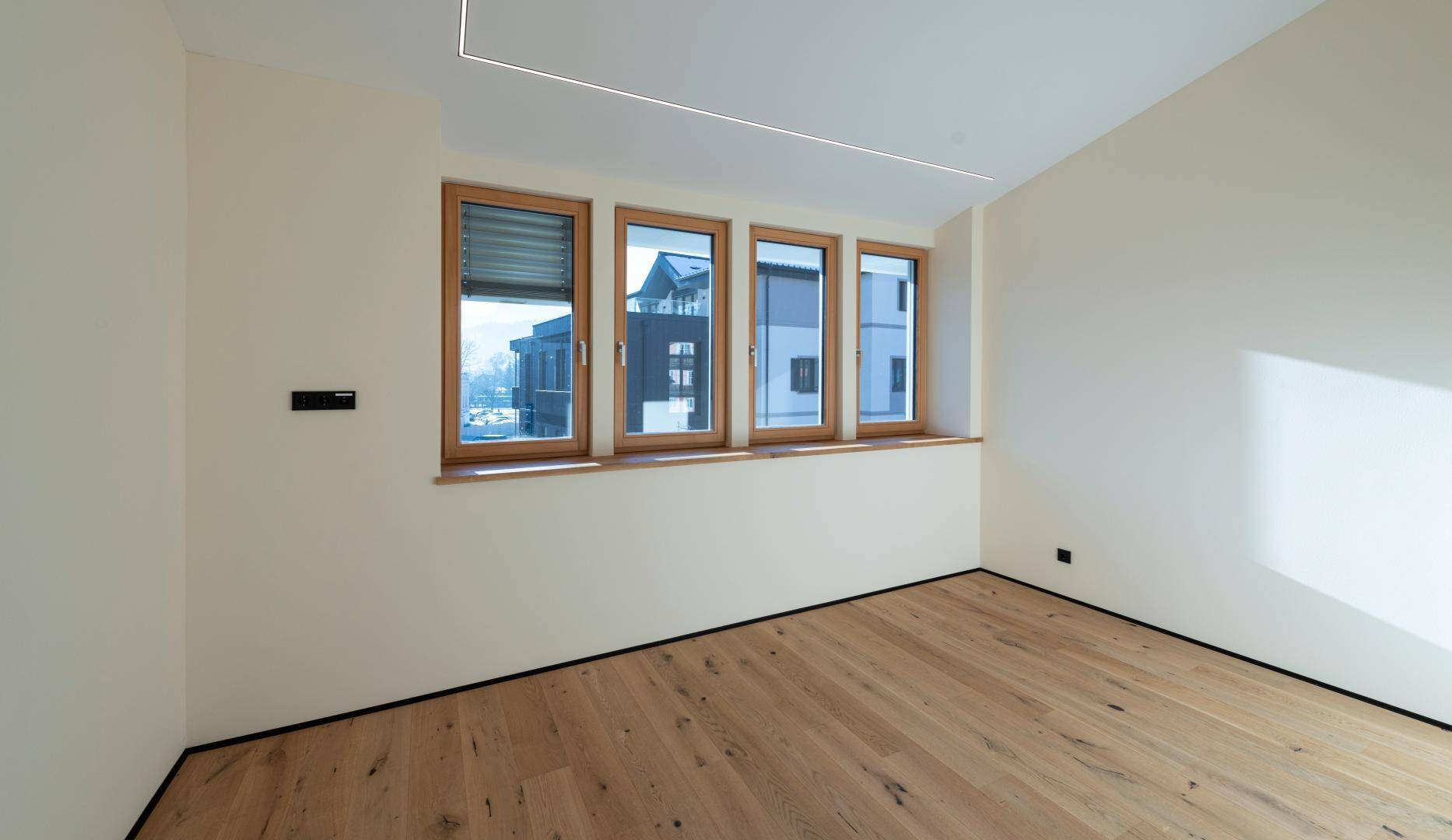 Heller Raum mit Holzboden, großen Fenstern und Blick auf die umliegenden Gebäude.