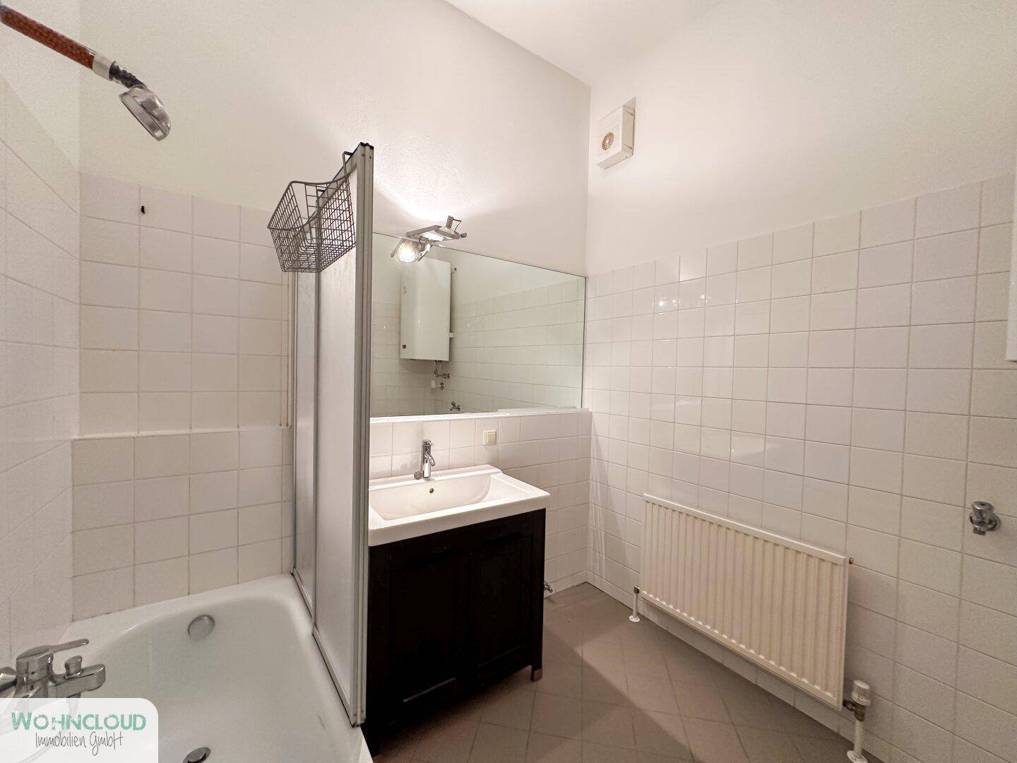 Badezimmer mit weißen Fliesen, Badewanne mit Duschabtrennung und Einzelwaschbecken.